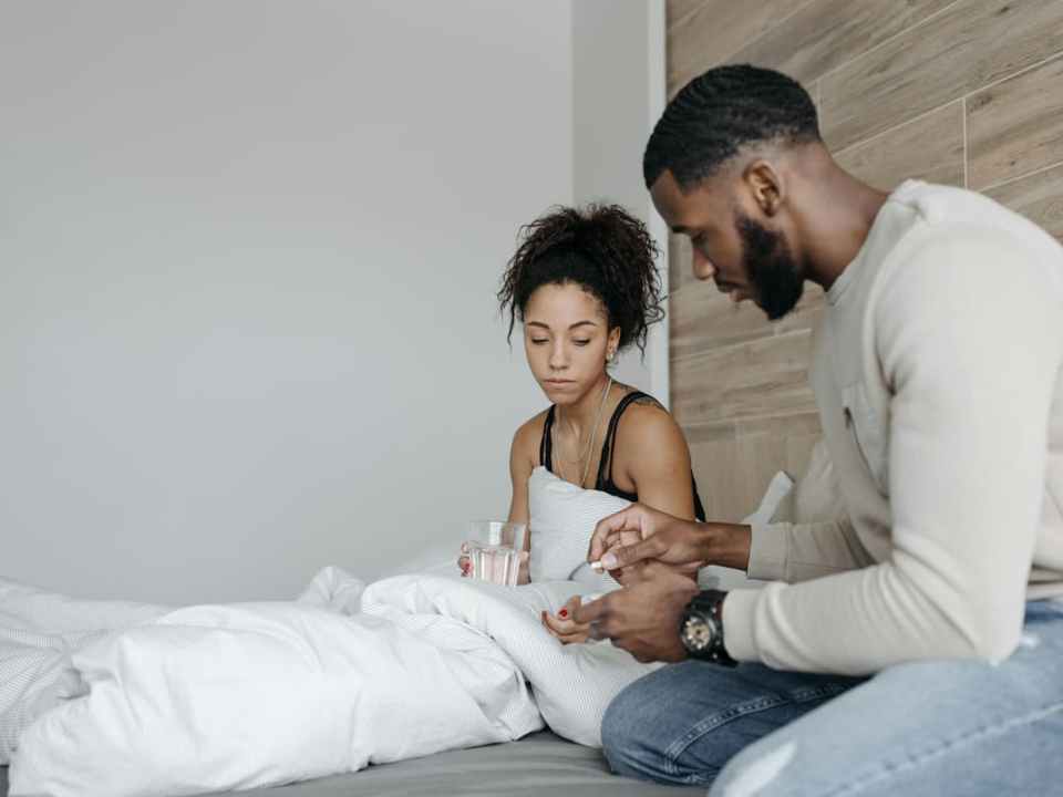 Homem dando remédio para tosse para mulher doente na cama.